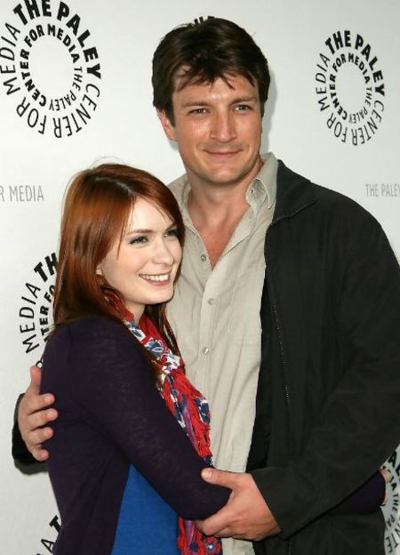 Nathan Fillion in black jacket and grey shirt poses a picture with Felicia Day.